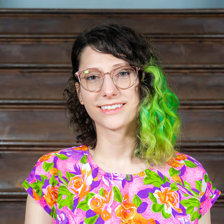 headshot of Kristyn in front of a staircase, smiling and wearing a pink shirt with an orange, blue, and purple floral pattern