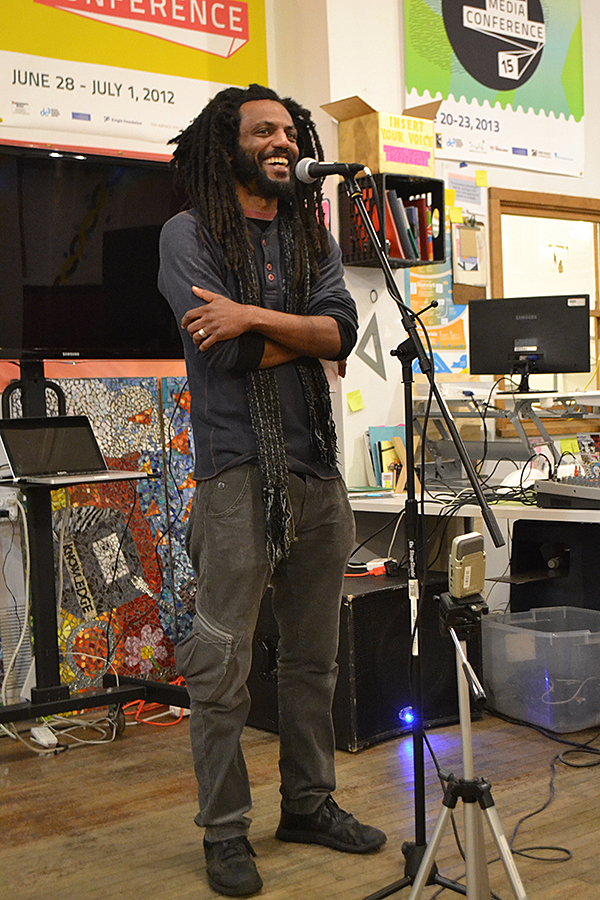 A man standing at a microphone, laughing, with arms crossed as he tells a story.